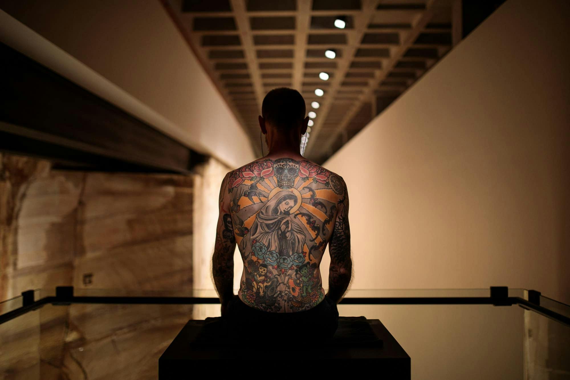 Tim sits in a plinth displaying his back of tattoos