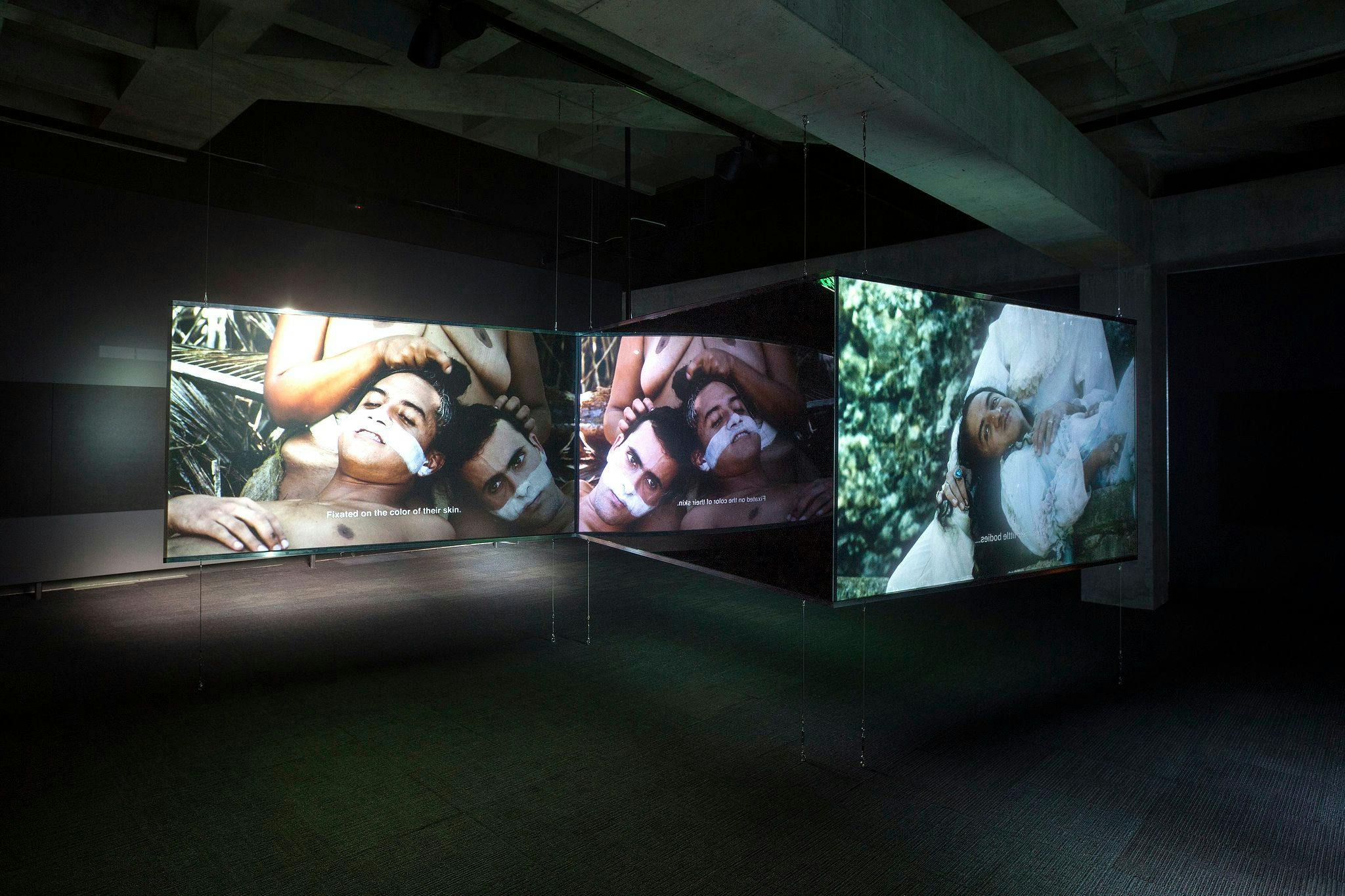 Dark exhibition space with three video screens in a zig-zag formation.