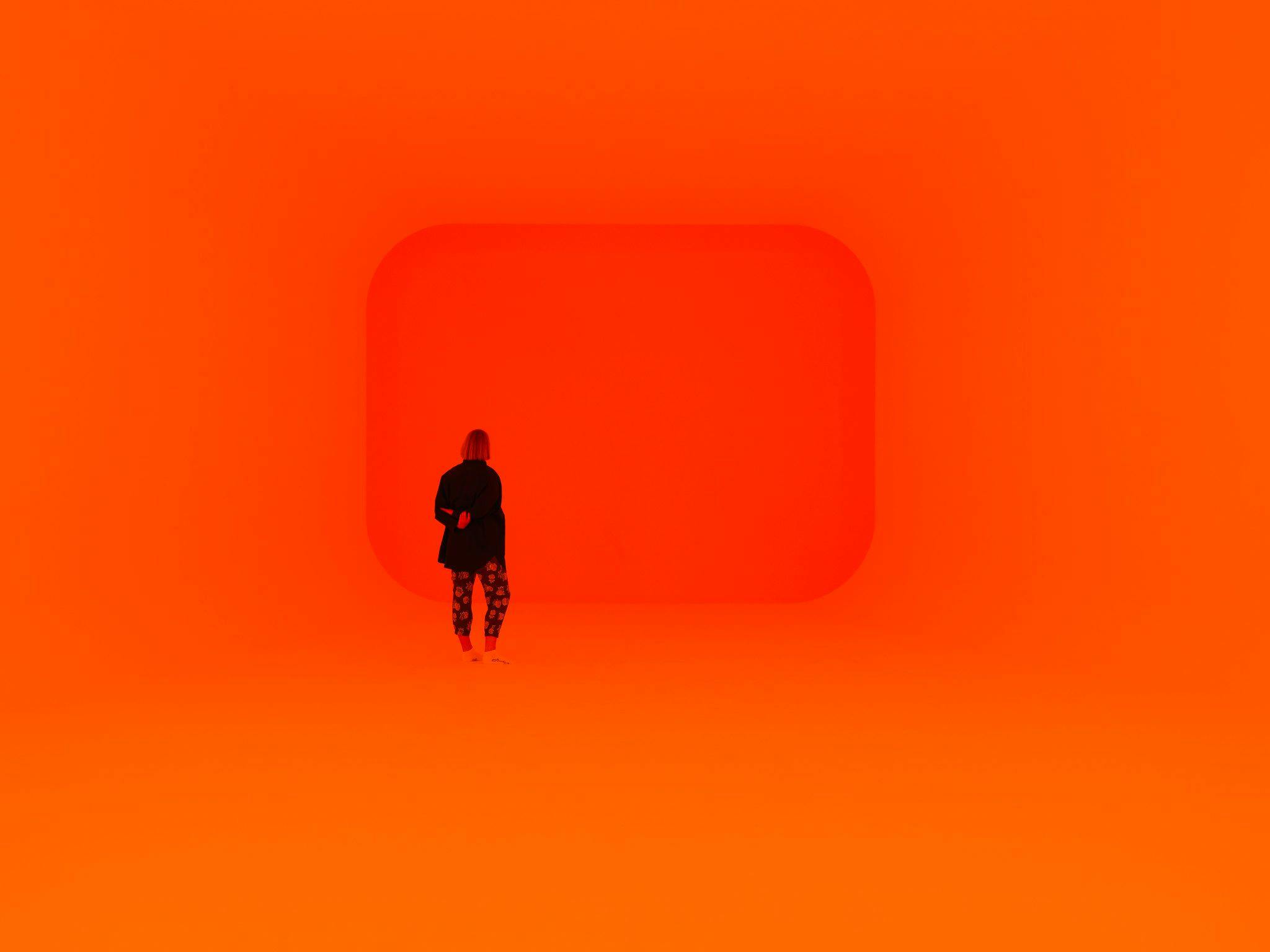 A figure stands in a room lit in hues of orange.