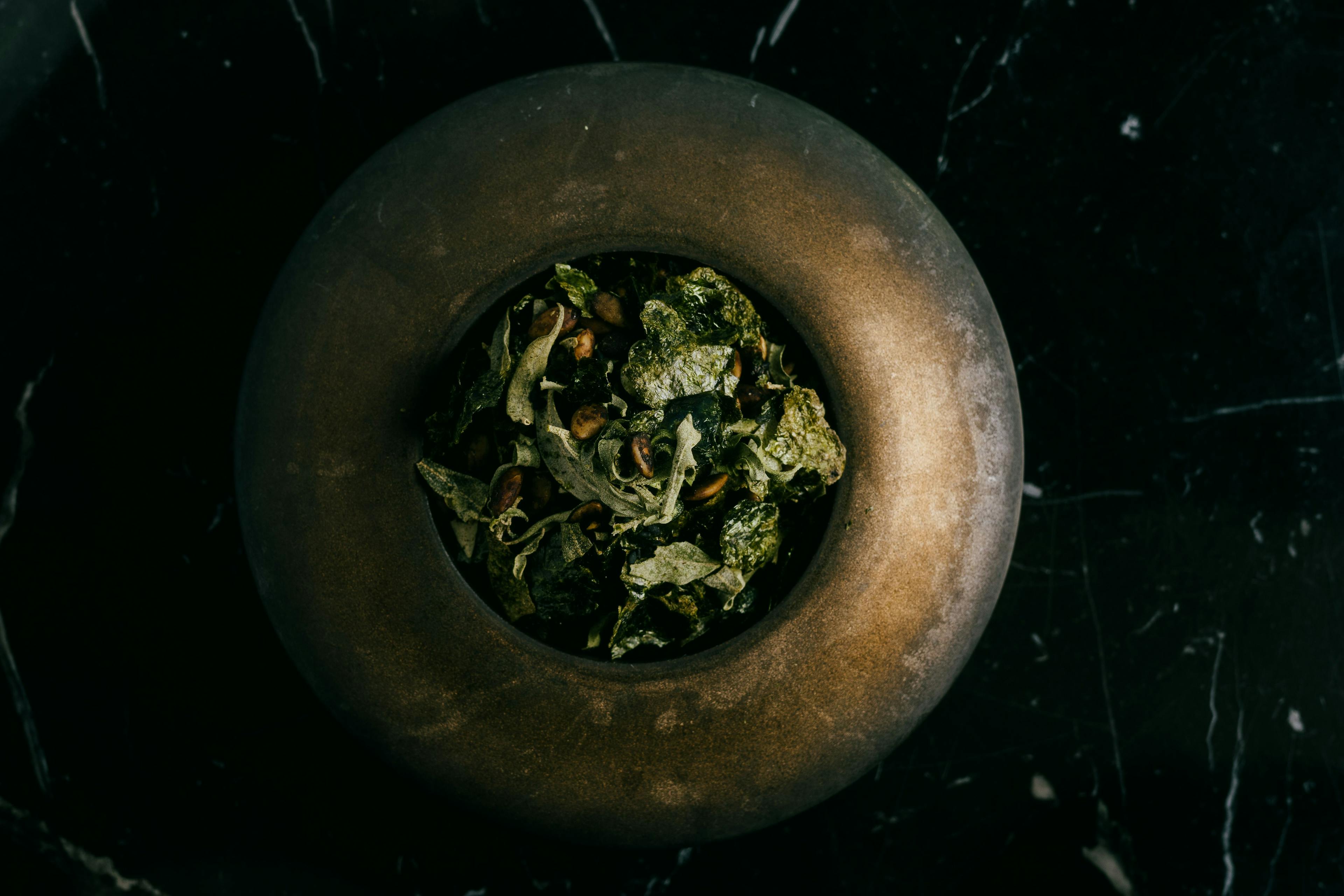 A dimly lit gold toned bowl with cripsy charred green vegetables