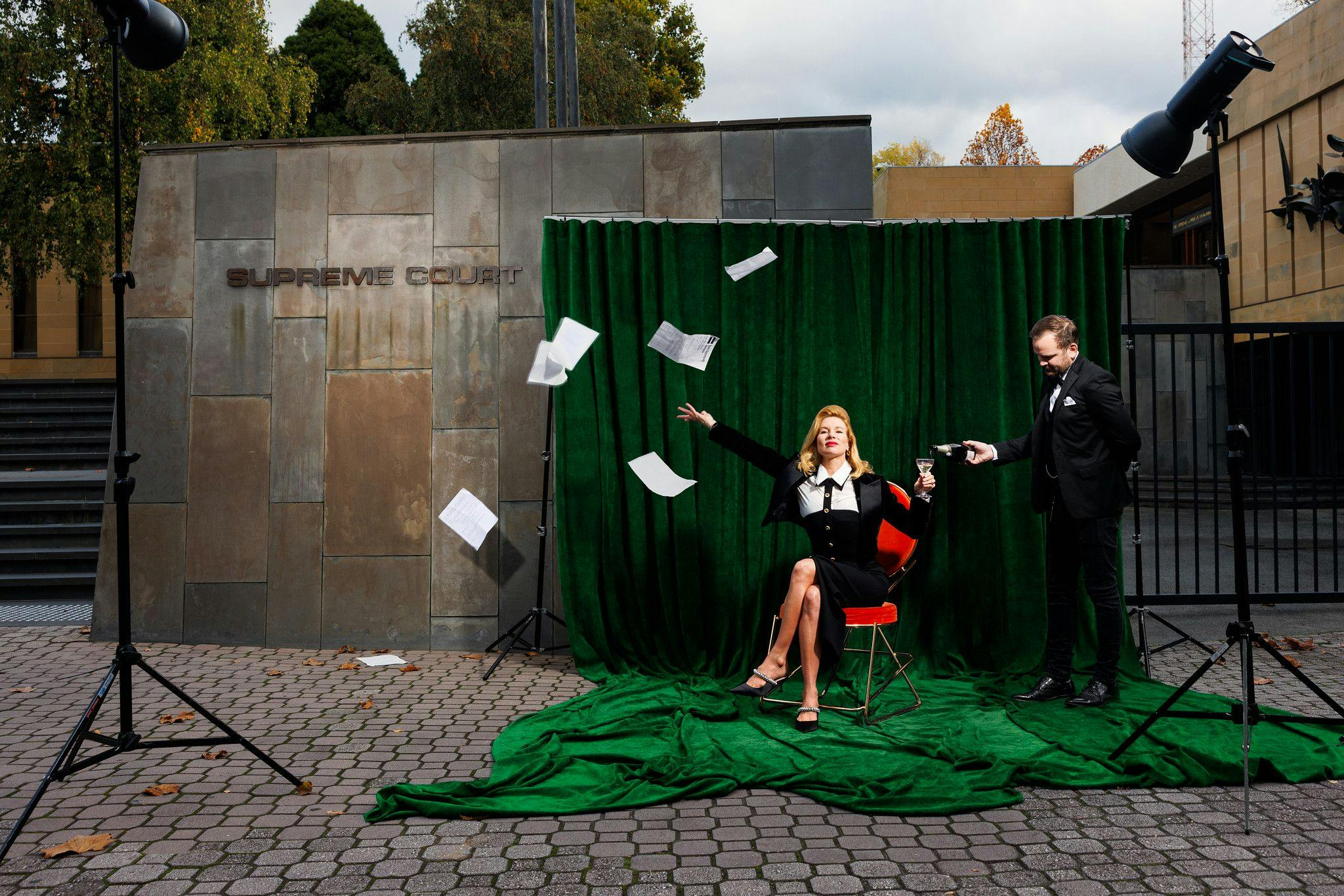 Kirsha in front of the Tasmania supreme court through documents in the air whilst being poured champagne by a male servant