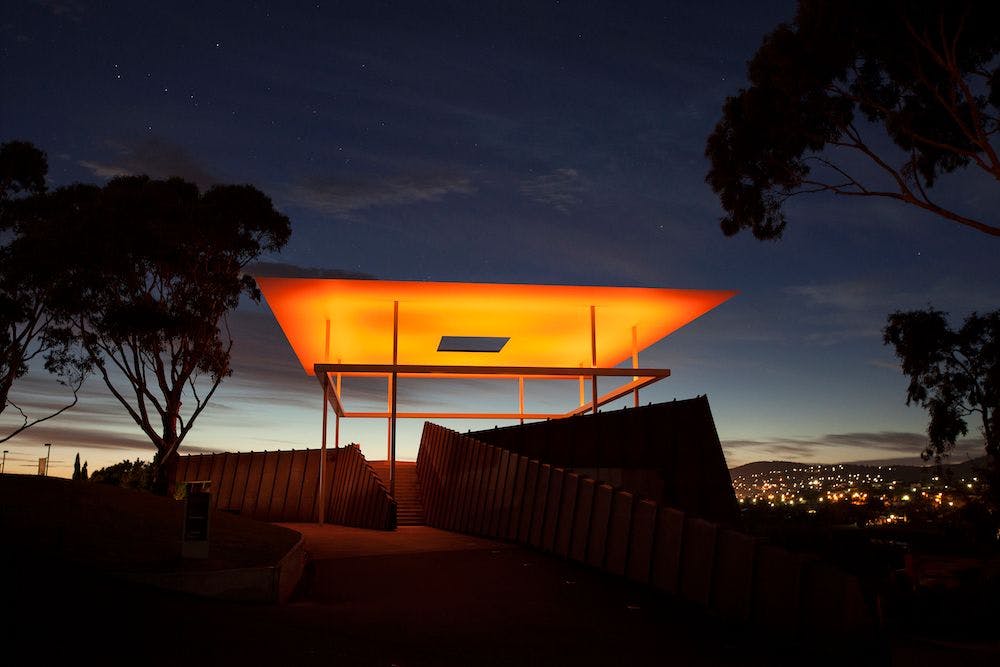 Sunsets behind a large structure lit in hues of orange and yellow.