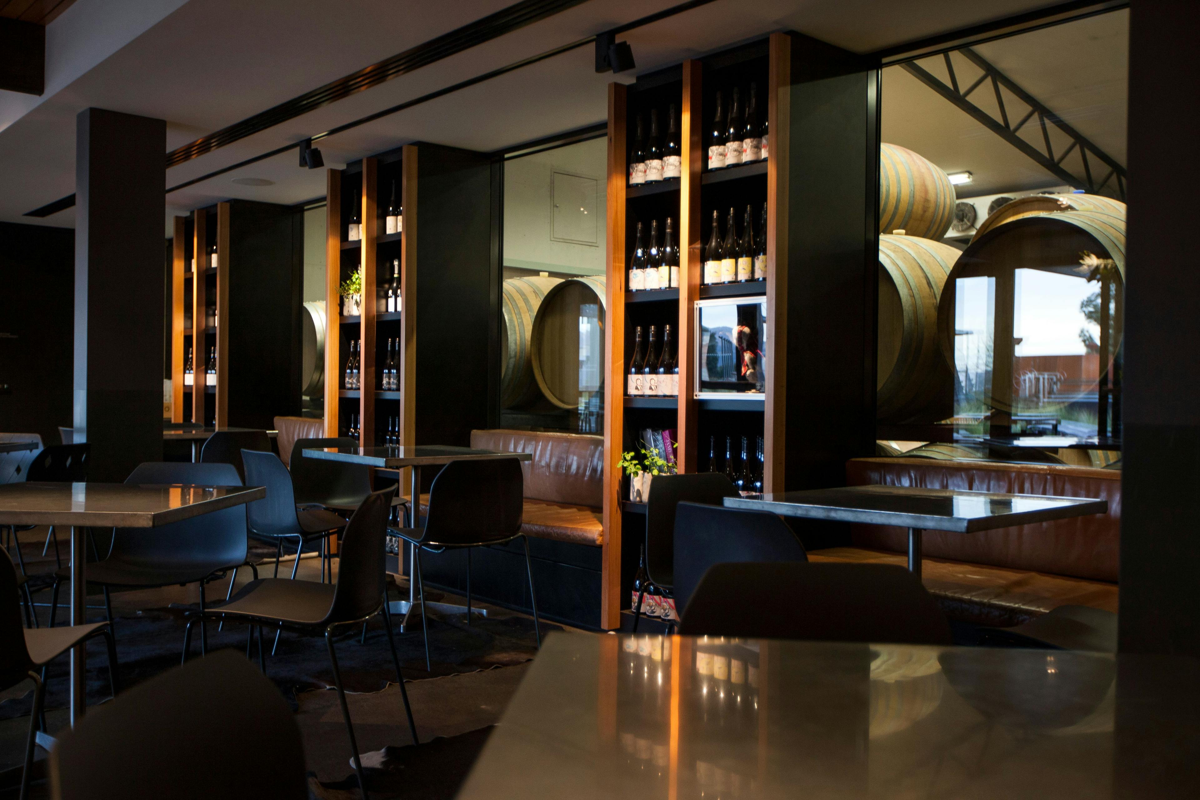 Internal image of the Wine Bar with leather bench seats, metal tables and wine barrells through the glass of the room next door