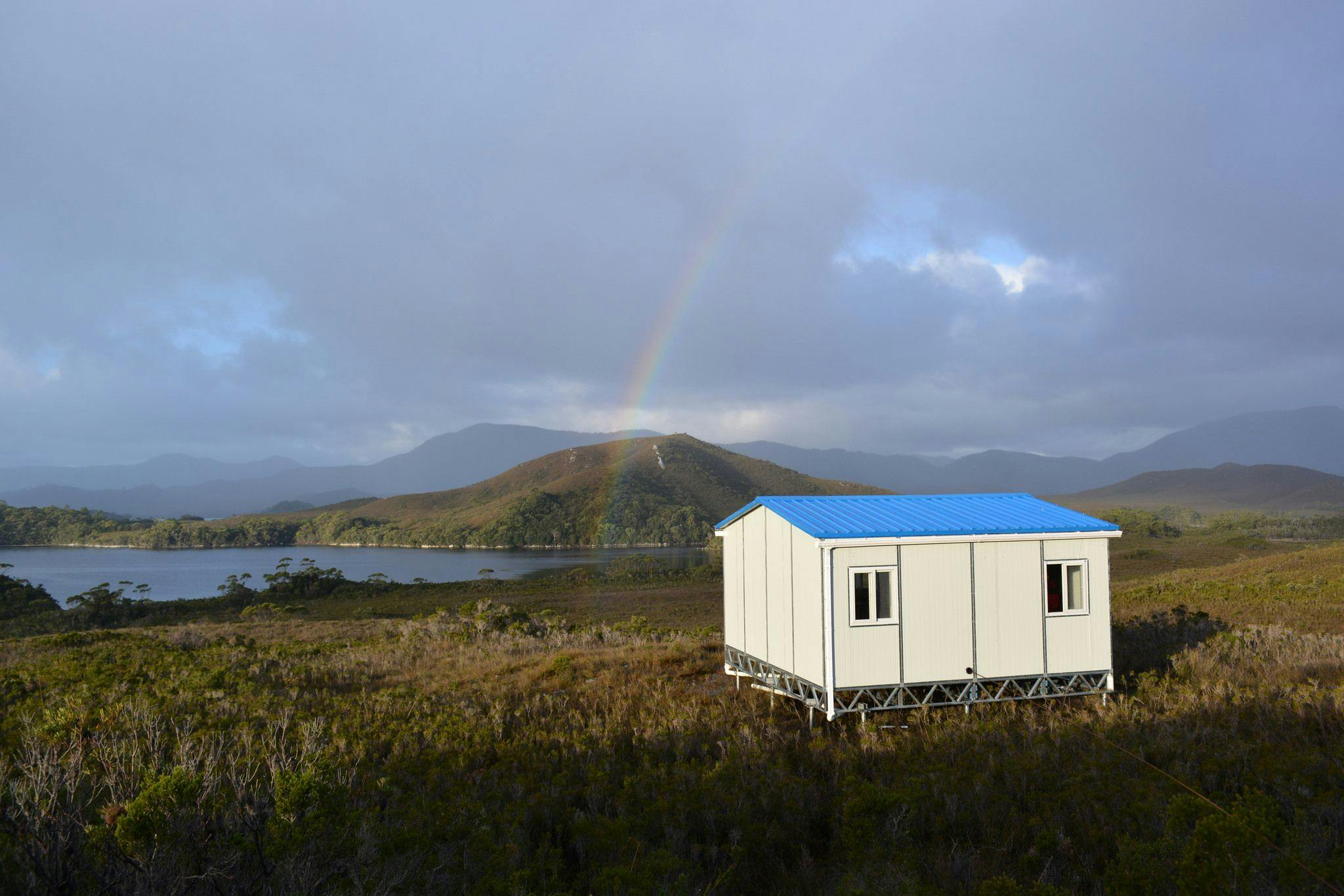 A temporary hut sitting in the isolated wilderness. A rainbow is in the distance.