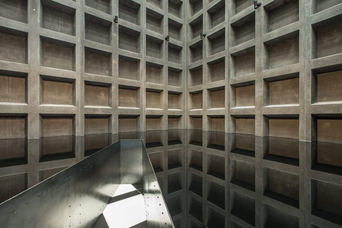 A concrete chamber of squares, sunlight shining in from above, and bottom half filled with engine oil.
