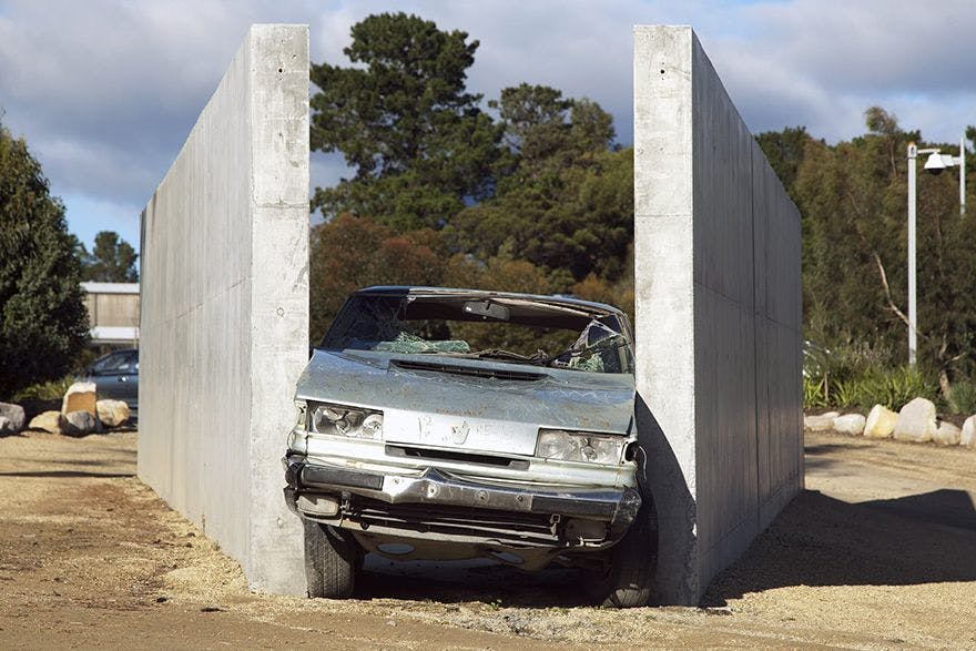 Front of a smashed car wedged between two parallel concrete walls.