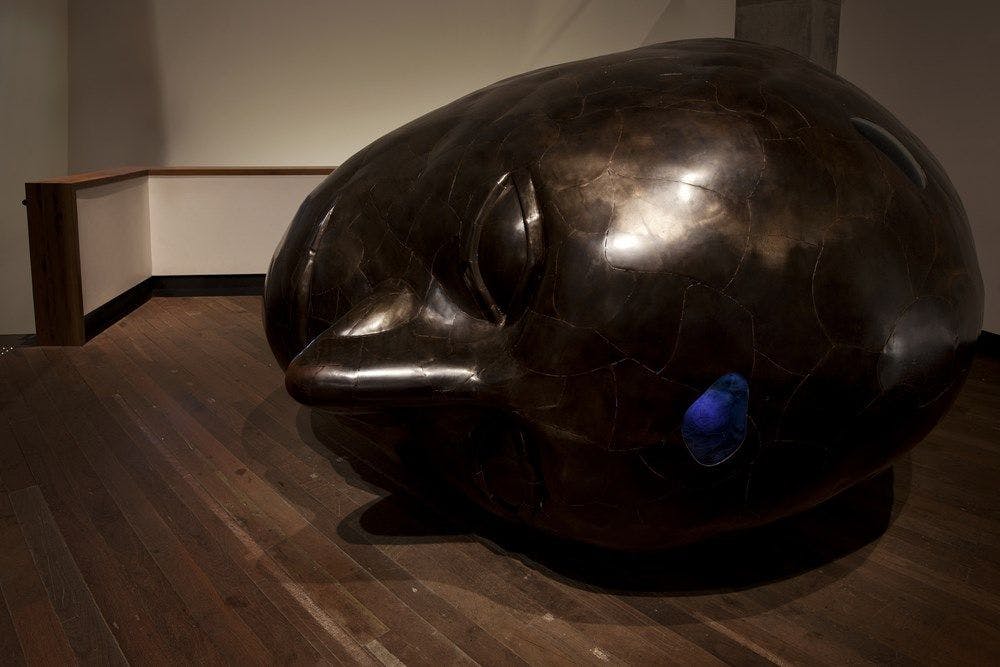 A large metal head lays on its side on a wooden floor.