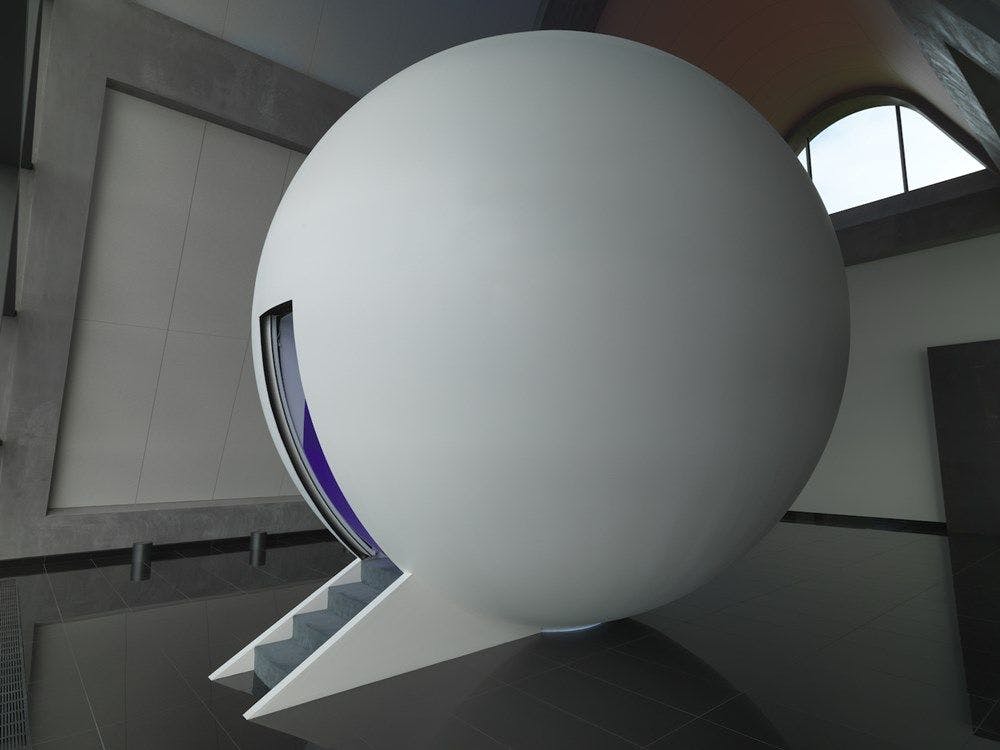 A large white sphere sits in a room with stairs leading into it.