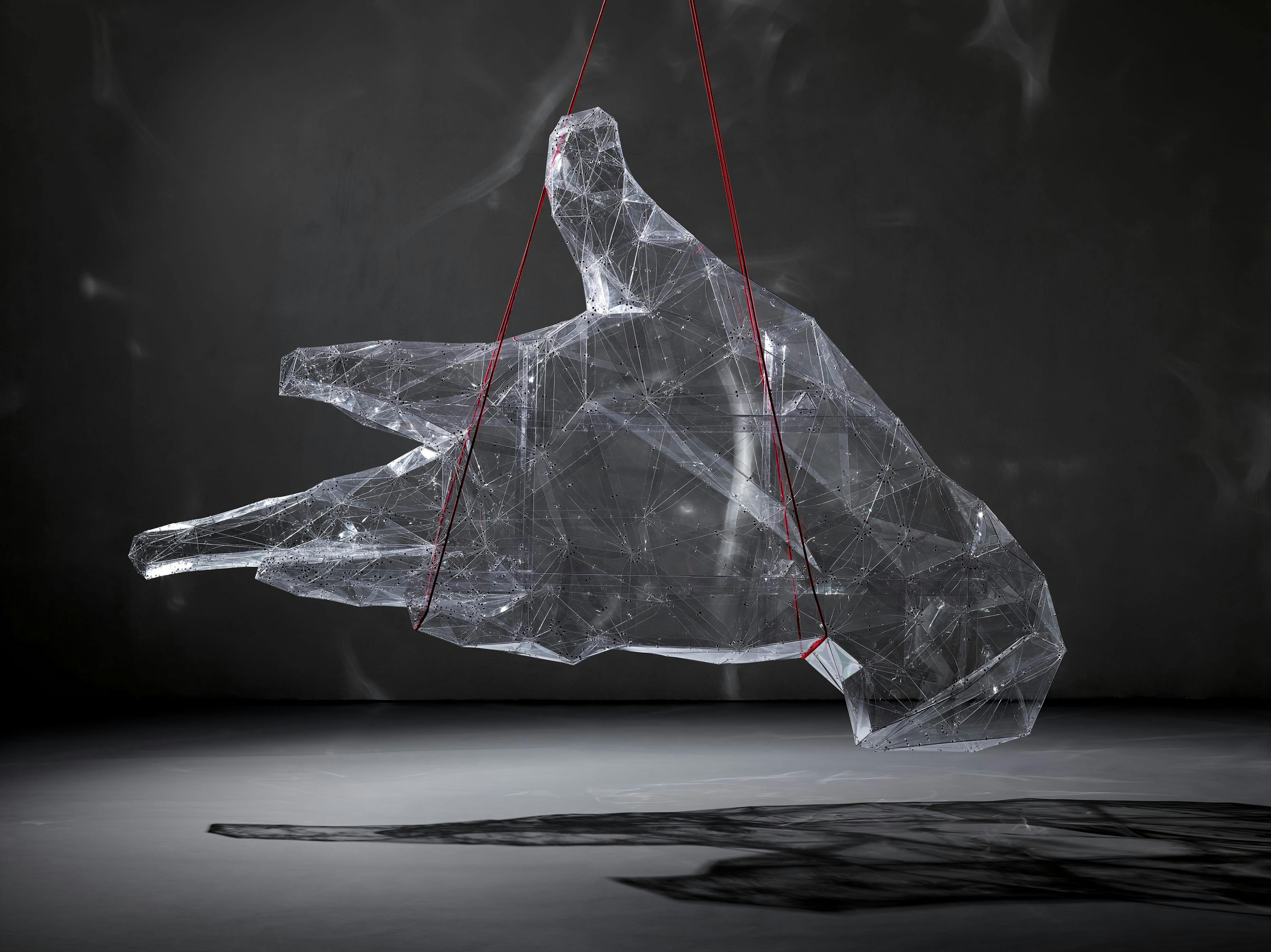Sculpture of a transparent hand suspended by red rope