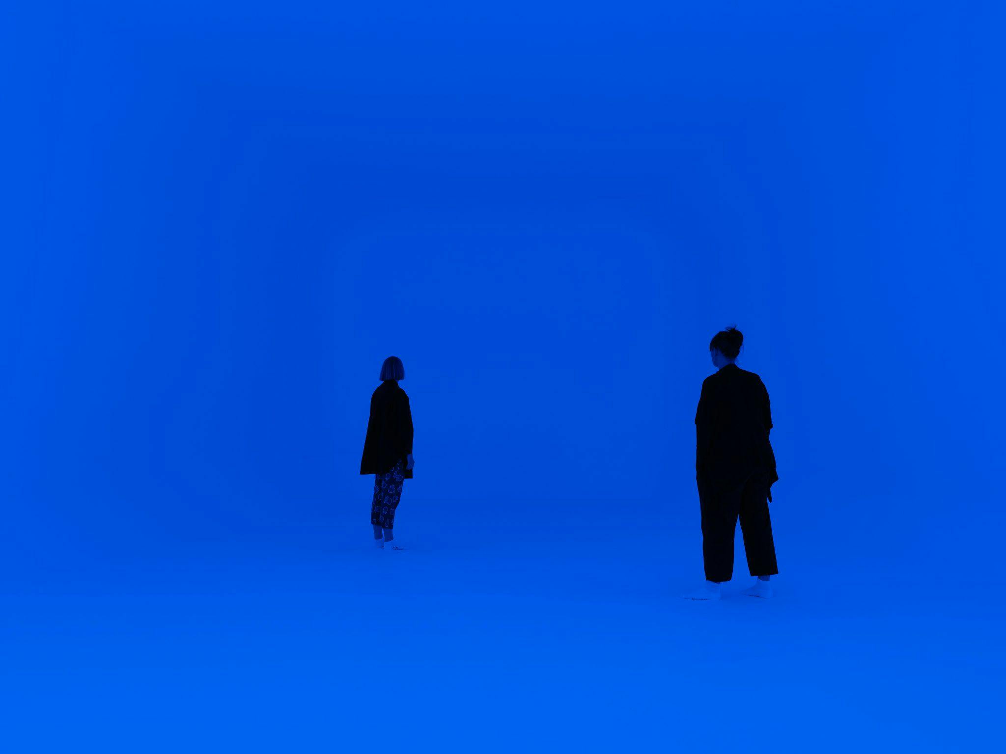 Two figures in a room lit in hues of blue.