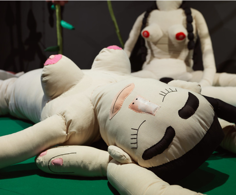 A large doll with naked breasts and striking black eye brows made of stitches and a calico like fabric