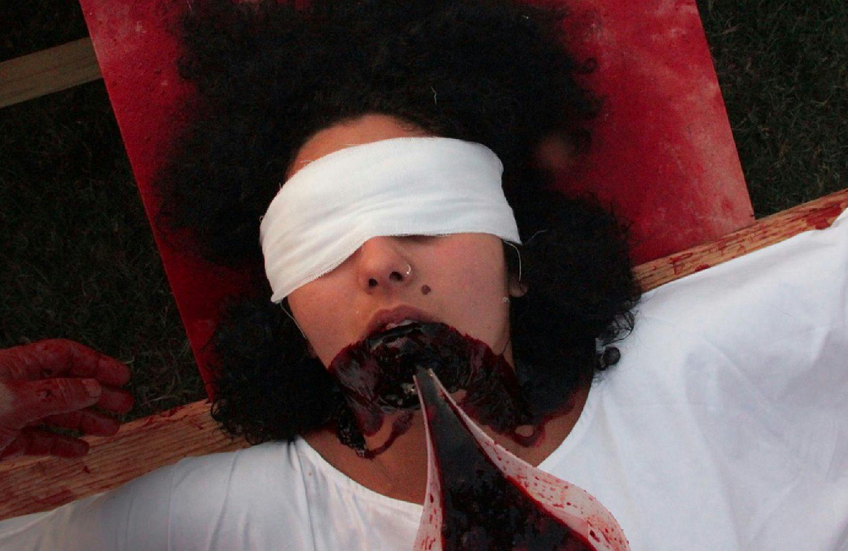A woman lays blind folded while blood is poured into her mouth overflowing onto her chin
