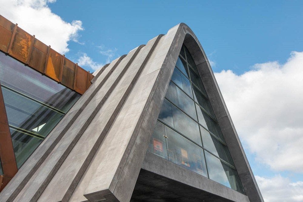 Photograph of a triangular building of concrete, glass and corten steel.
