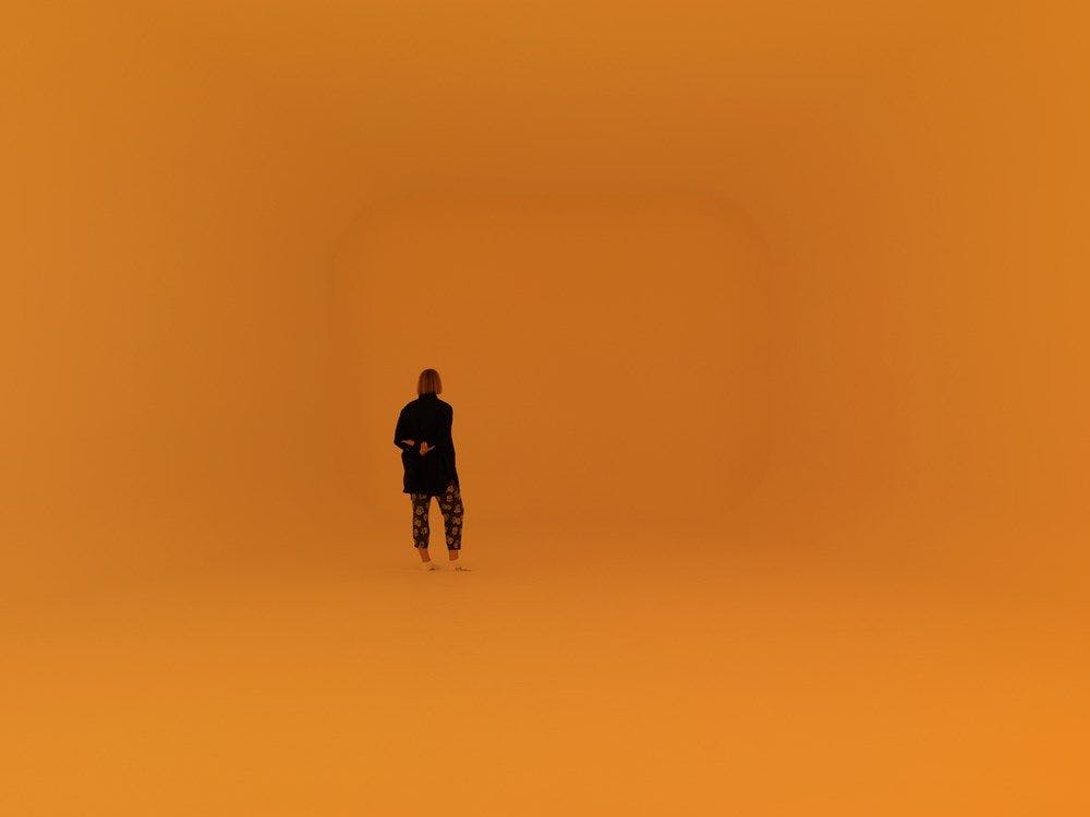 A figure stands in an ambient room lit orange.