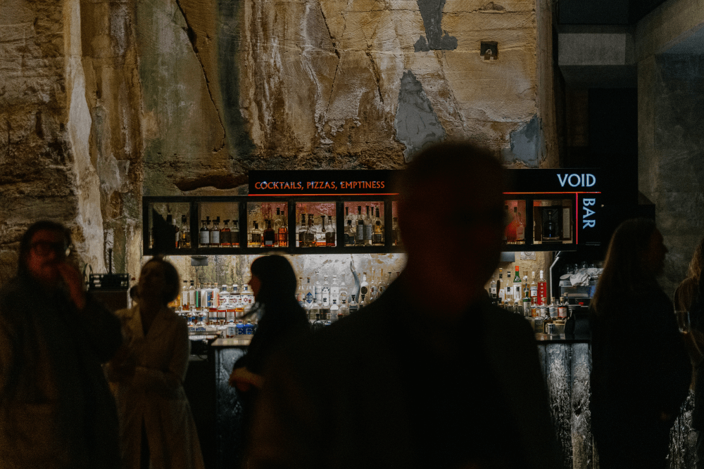 Silhouettes of people in front of the Void bar with large sandstone walls behind