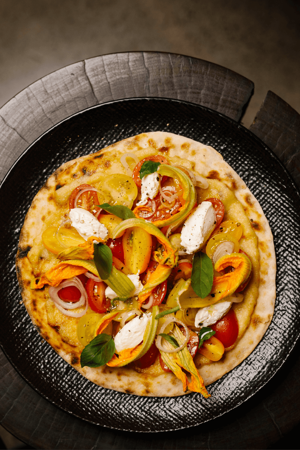 a plate of yellow summer tomatoes, fresh basil and mozzarella on a flat bread