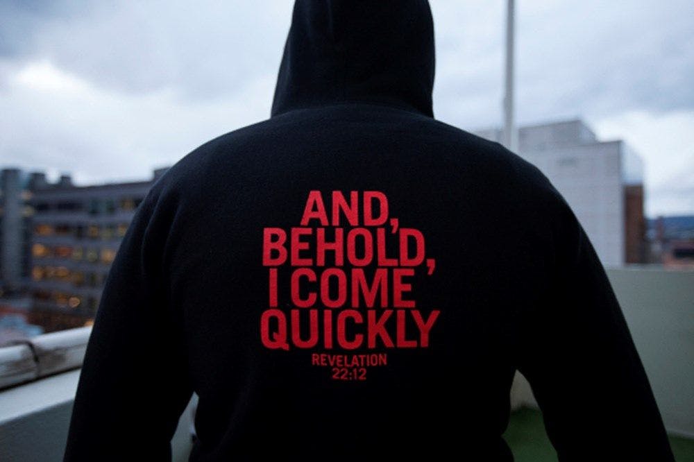 Back of a figure in a black hooded jumper with red text "And, behold, I come quickly"