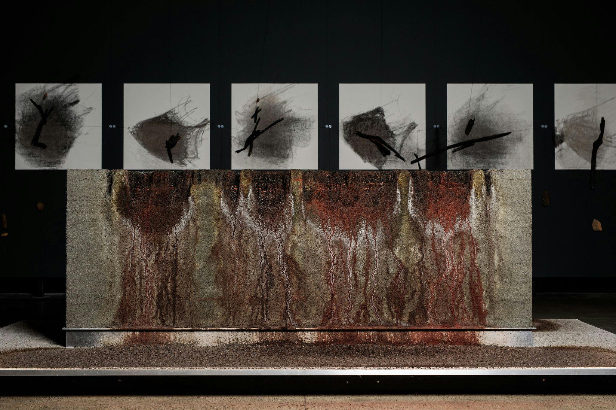 6 charcoal drawings made by a mechanical plotting system. Water erosion stains a plinth of compacted soil.