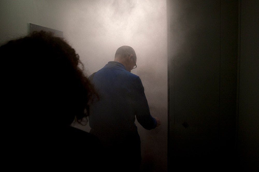 Two people enter a smokey dark room.