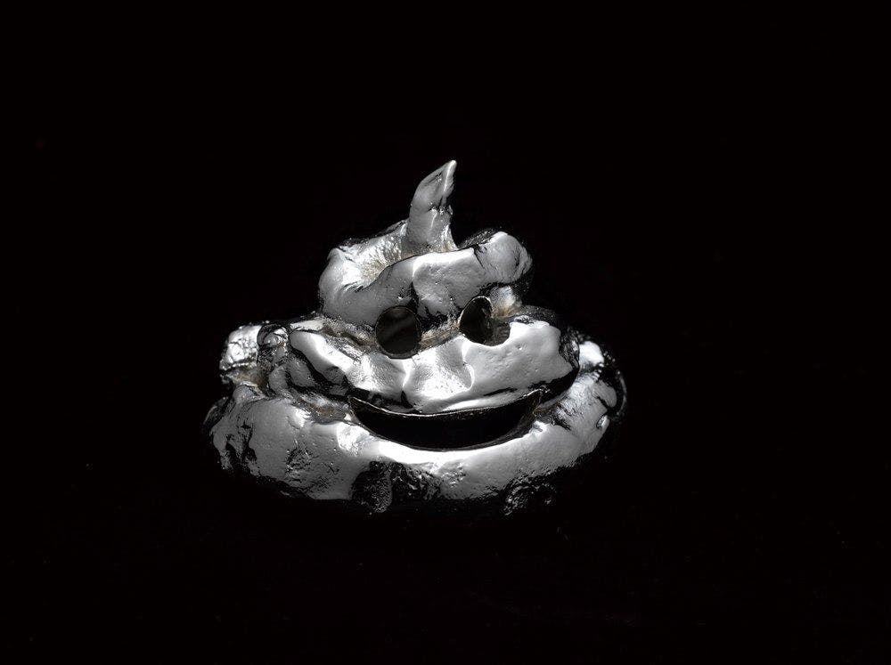 A silver poo shaped sculpture with a smiley face on a black background.