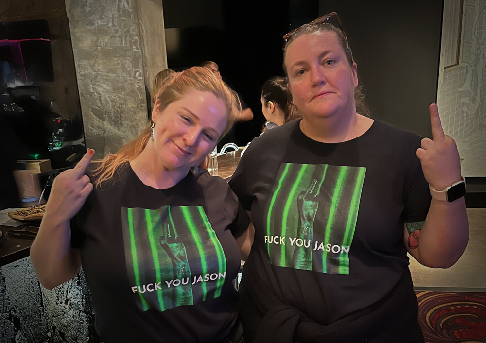 Two visitors wearing t-shirts that read "Fuck you Jason" and showing their middle fingers toward the camera