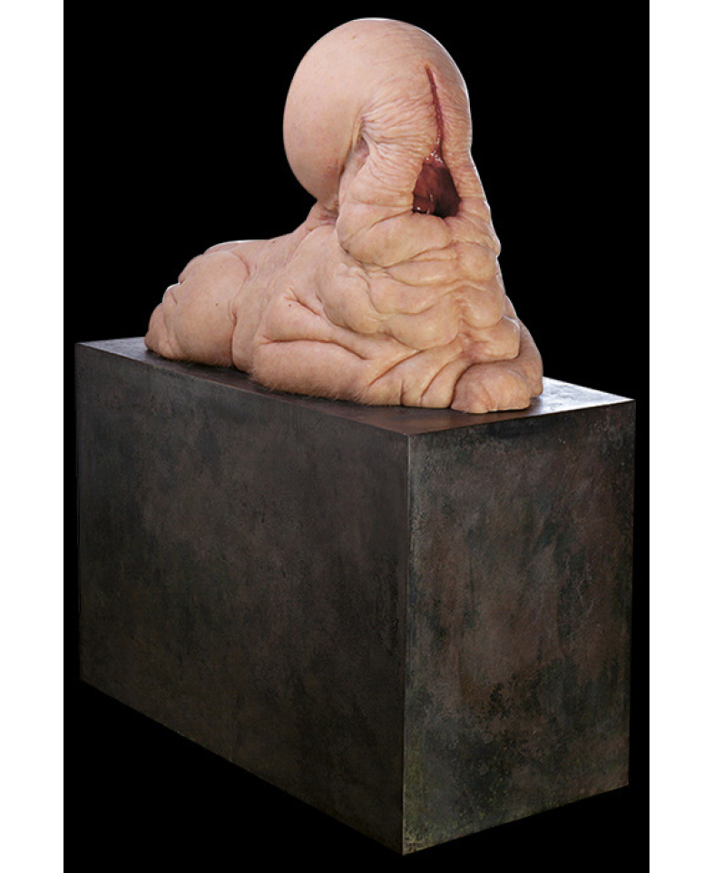 A pink, fleshy sphinx like sculpture with a gaping maw atop a plinth.