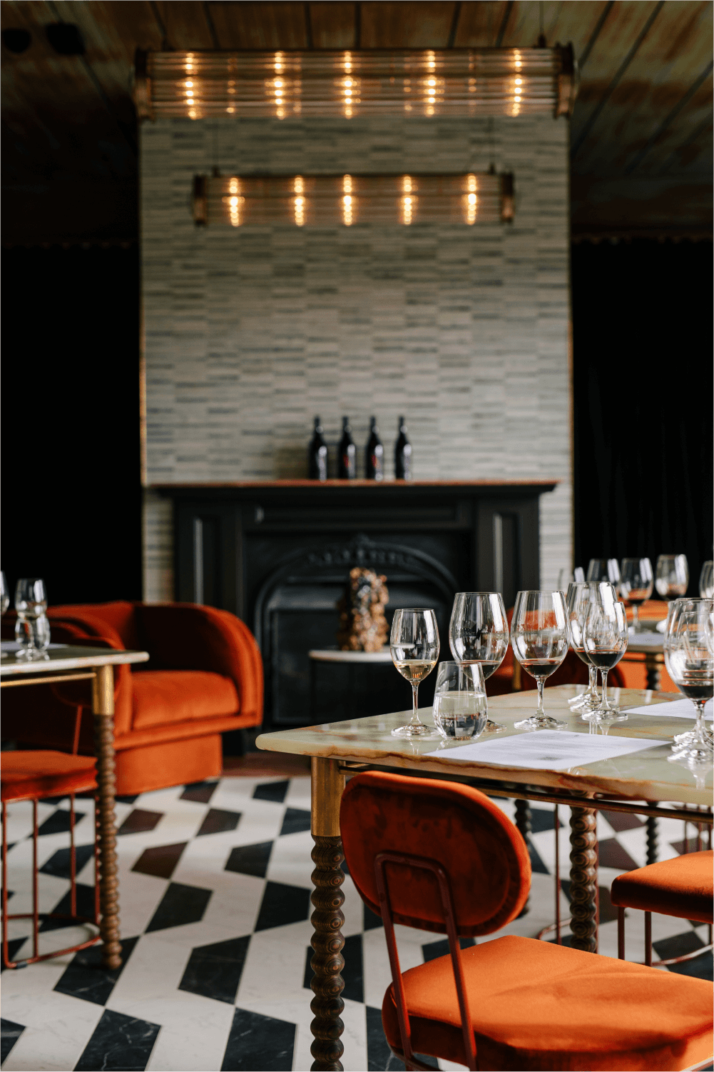 Interior of Domaine A. A fireplace, soft lighting, orange velvet chairs and marble table tops with glasses filled ready for tasting