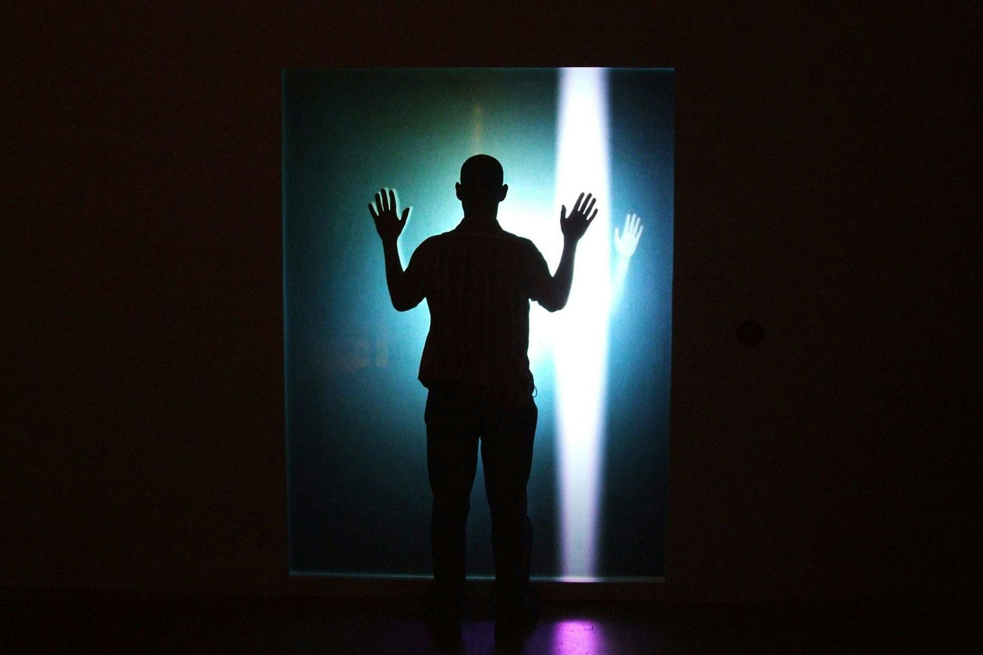 Silhouette of a person standing with their hands up in front of a line of bright light.