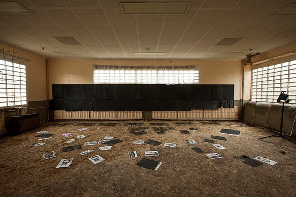 A dirty light room with grills on the windows. Numerous charcoal drawers are scattered around the floor.