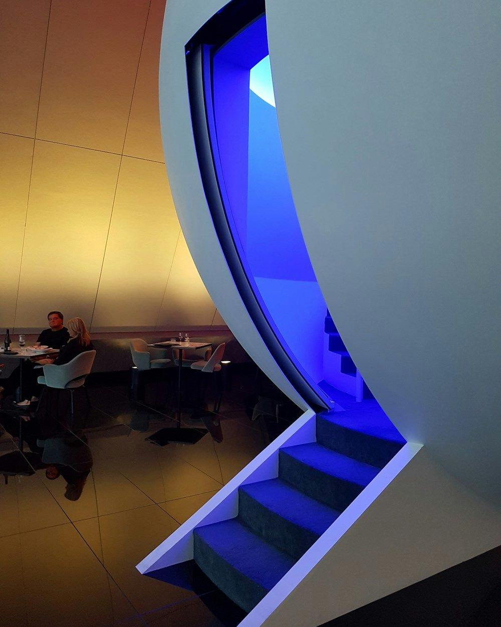 A blue toned staircase into a white sphere within a restaurant.