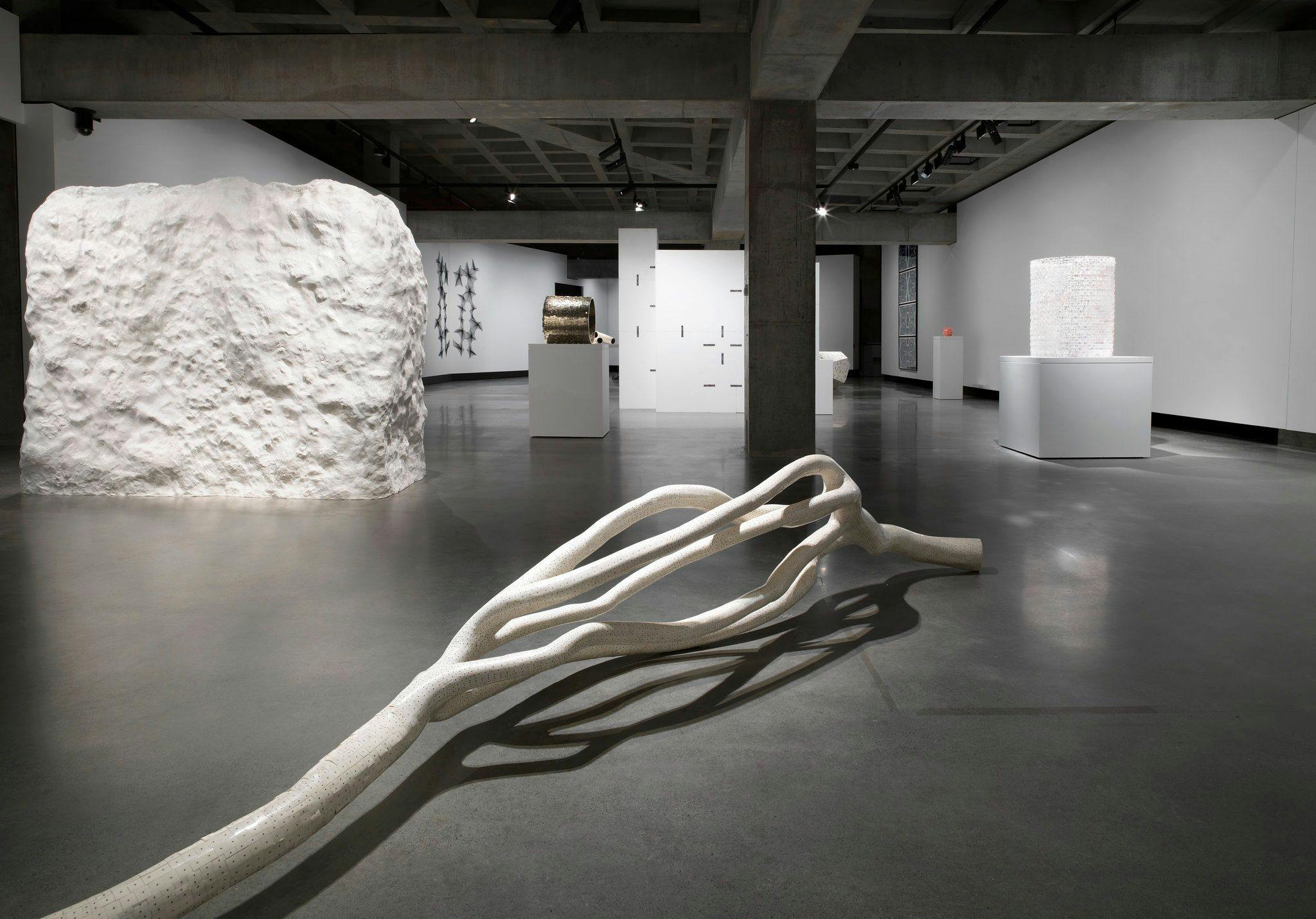 Exhibition view of a white coral like sculpture lying on the ground. And a large white textured cube.