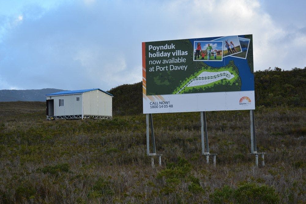 A billboard advertising land sale in front of a temporary housing in the wilderness.