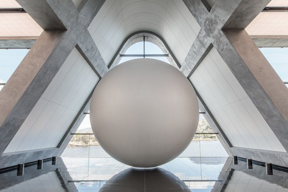A large white sphere sits on a reflective floor in a triangular room.