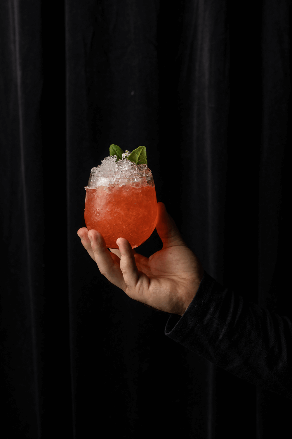 A hand holds a refreshing looking cocktail filled with ice