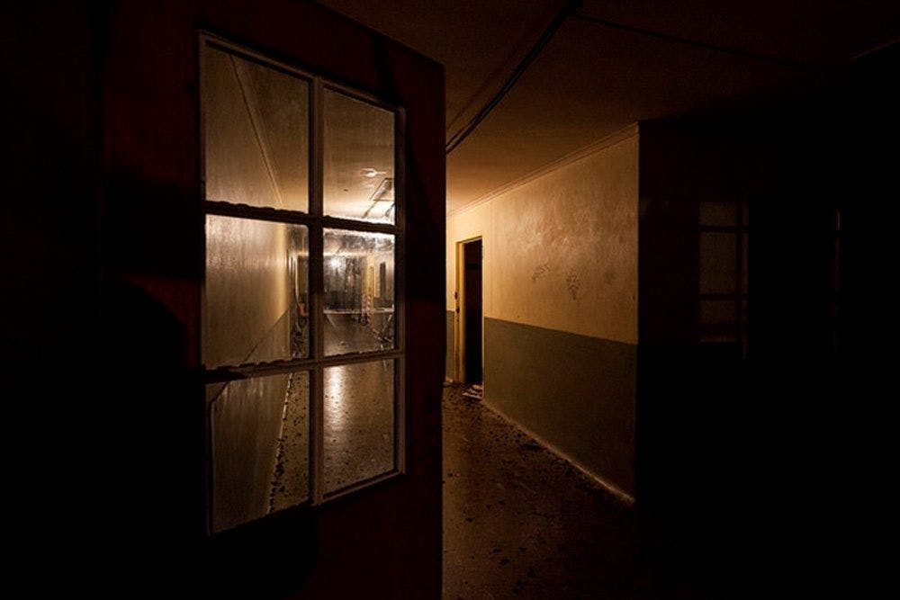 A view down a dark corridor through a half open windowed door. A warm light is on down the far end of the space.