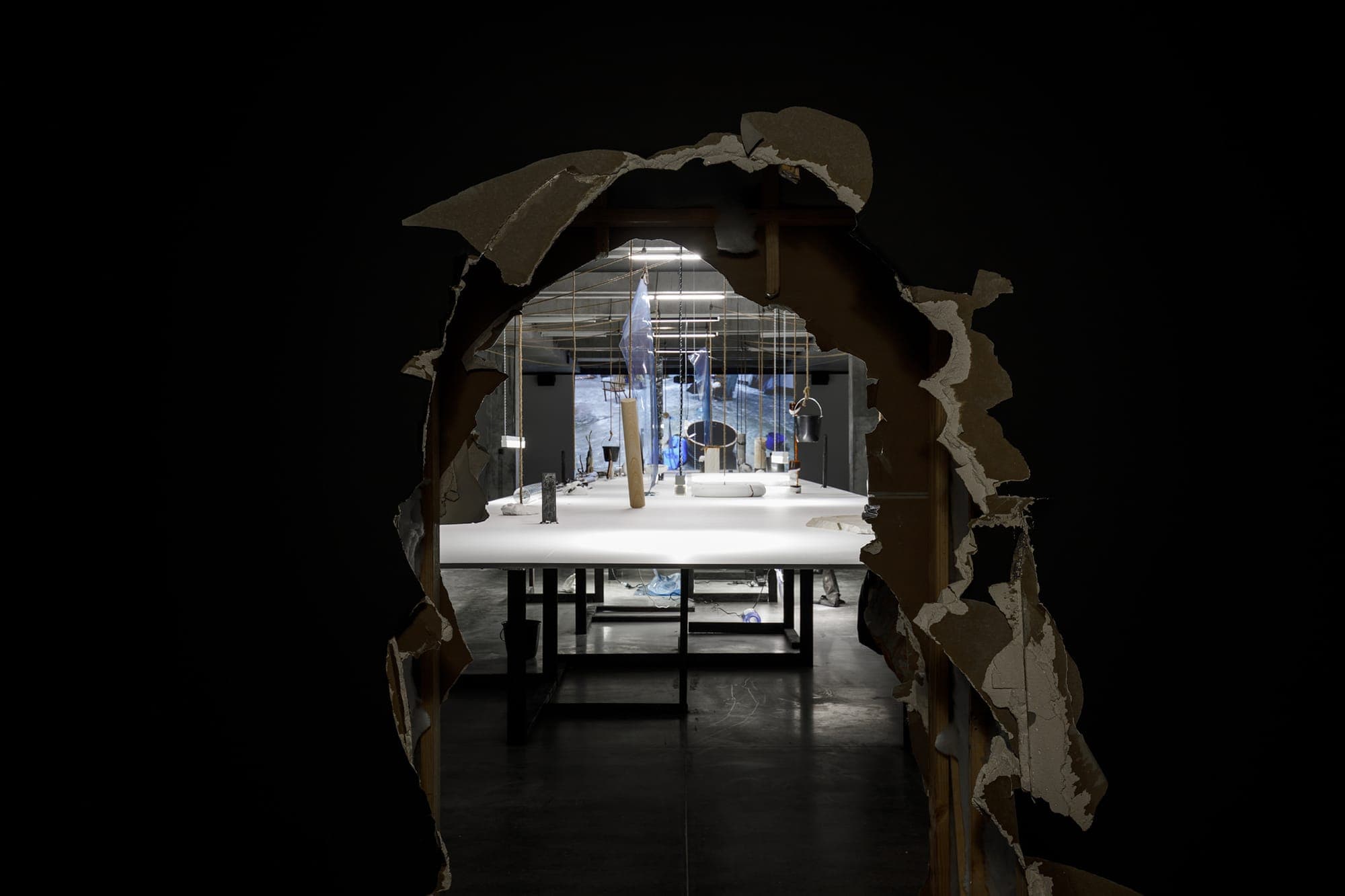 White benches with objects suspended viewed through a broken wall