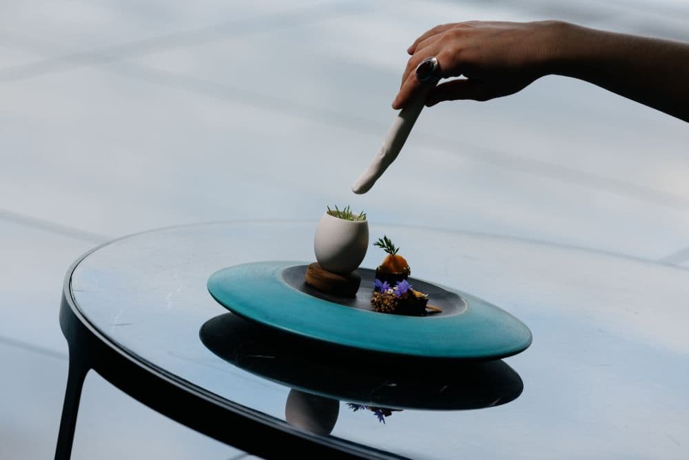 A egg shaped vessel on a blue plate of delicacies.