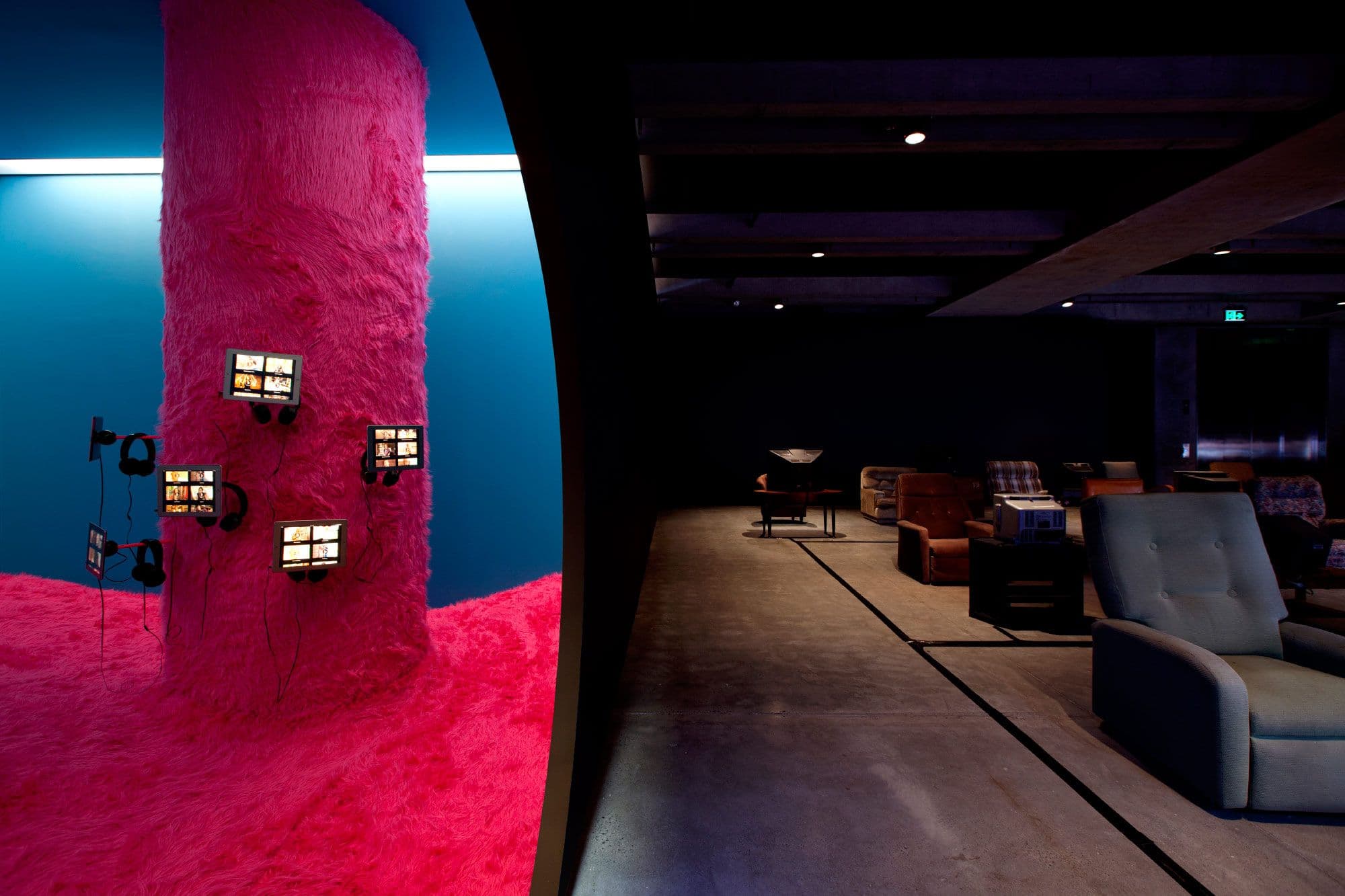 A bright pink fuzzy pole with tablets and headphones hanging off it. To the left of that room, a dark space willed with old lounge chairs and CRT televisions.